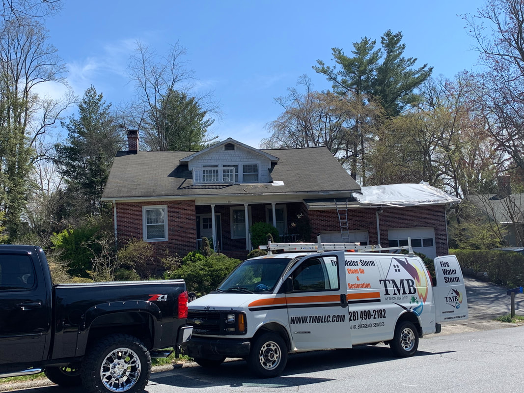 TMB Restoration service van parked in front of a residential home with visible roof damage and protective tarp, indicating active storm or structural damage restoration response.